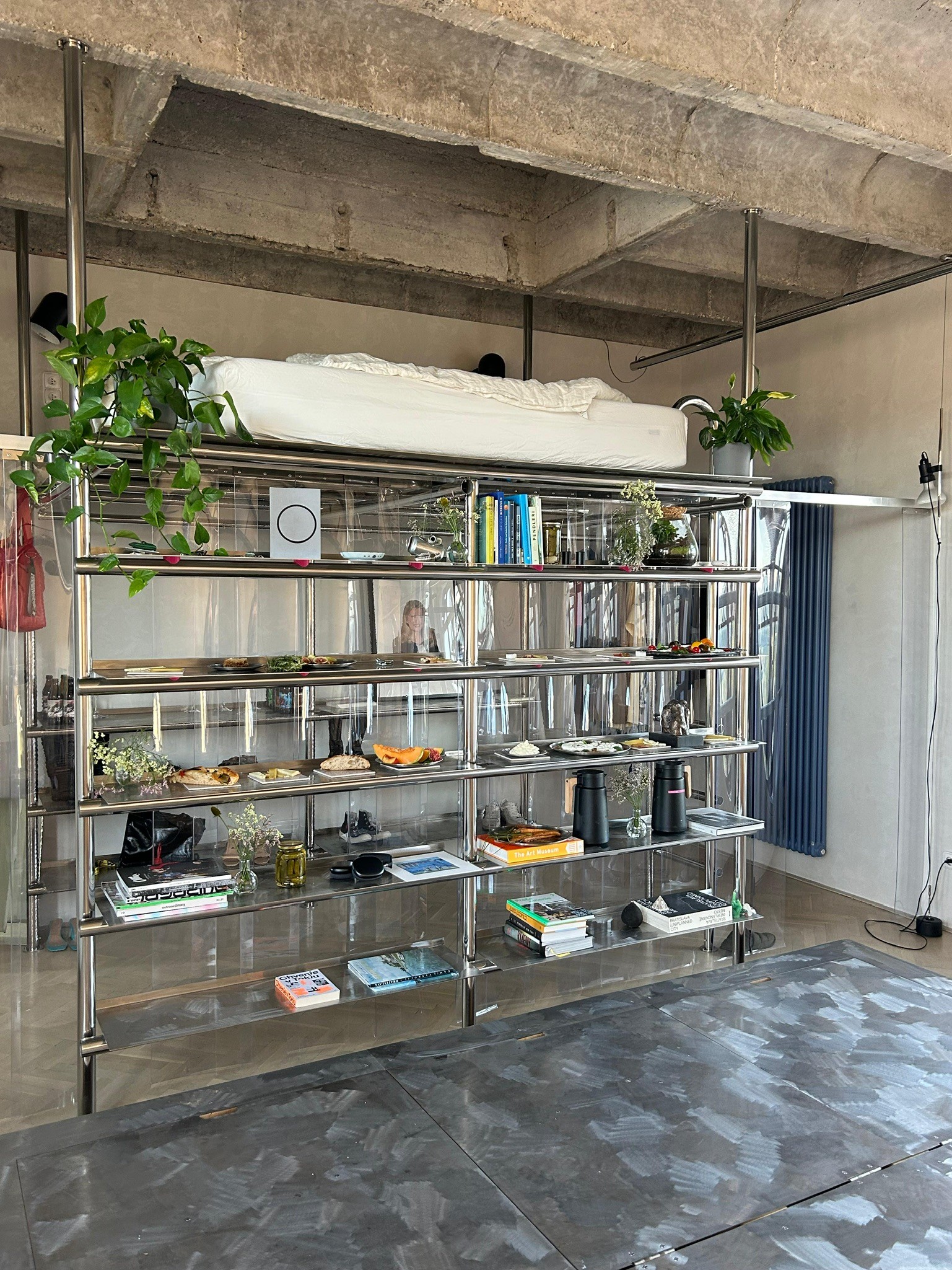 View of the Kotva Space interior — modular shelves, concrete floor, and circular window with the Kotva logo reflected.