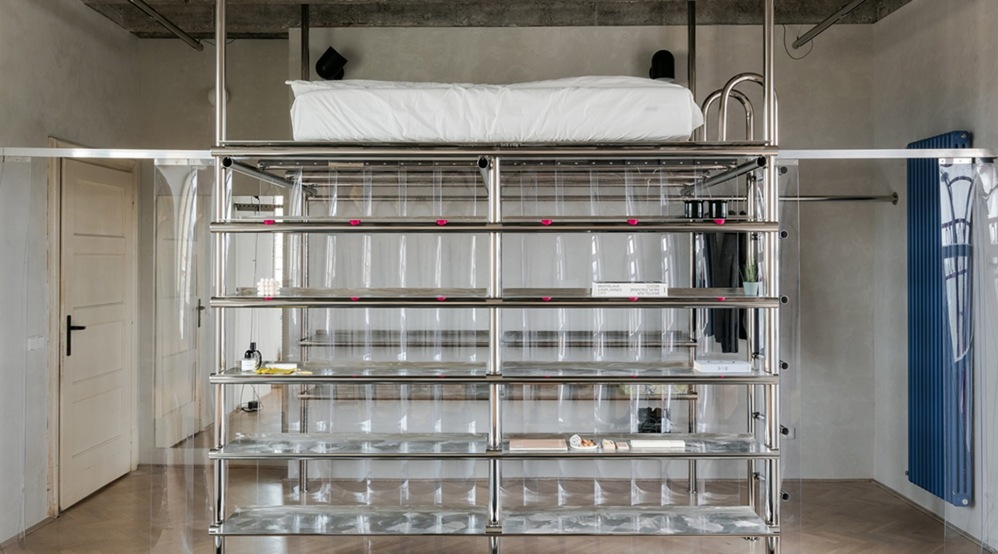 View of the Kotva Space interior — modular shelves, concrete floor, and circular window with the Kotva logo reflected.